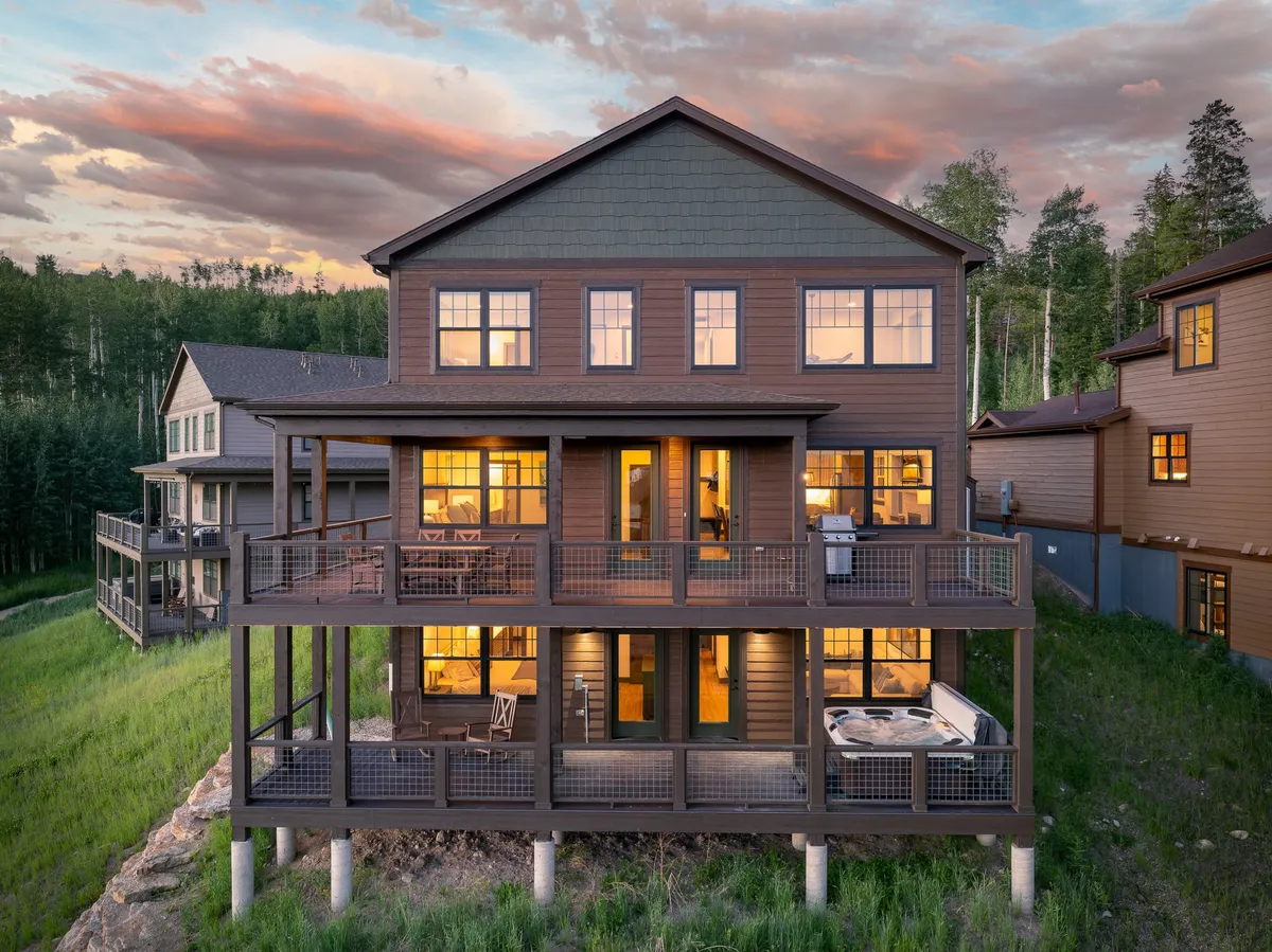 This exterior image features a spacious deck with a luxurious hot tub, large windows reflecting the natural surroundings, and contemporary architecture nestled among trees—a perfect base for relaxing after outdoor adventures.
