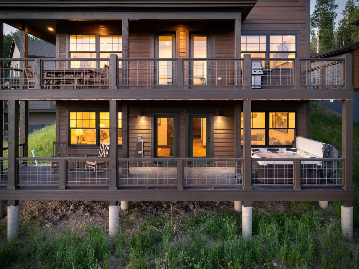 The image features a cozy balcony with comfortable seating and a hot tub, set against large windows that emit warm, inviting light. The balcony offers a relaxing spot to soak and unwind while taking in evening views of the surroundings, suggesting both privacy and luxury in an outdoor setting.