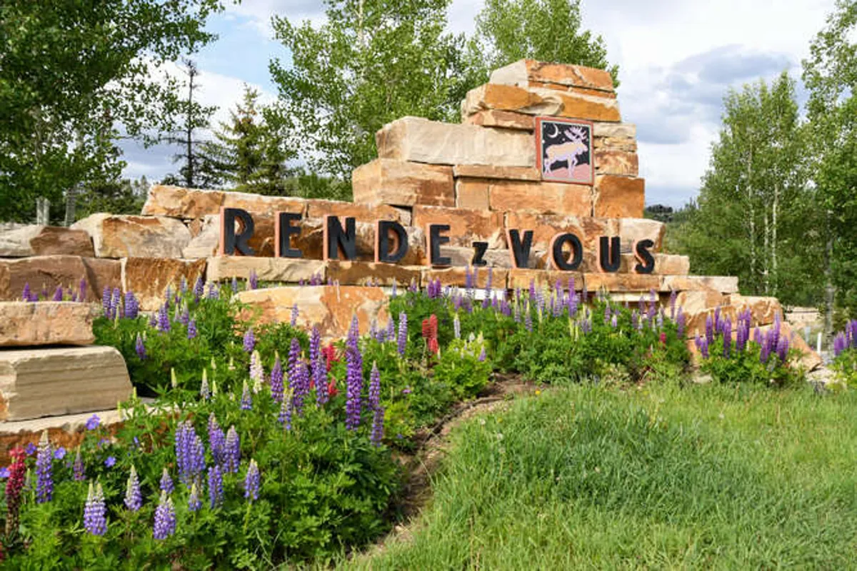 The welcoming entrance of the Rendezvous Community, marked by a stone monument surrounded by vibrant flowers and natural landscaping. The signage and inviting setting evoke a sense of arrival and community pride.