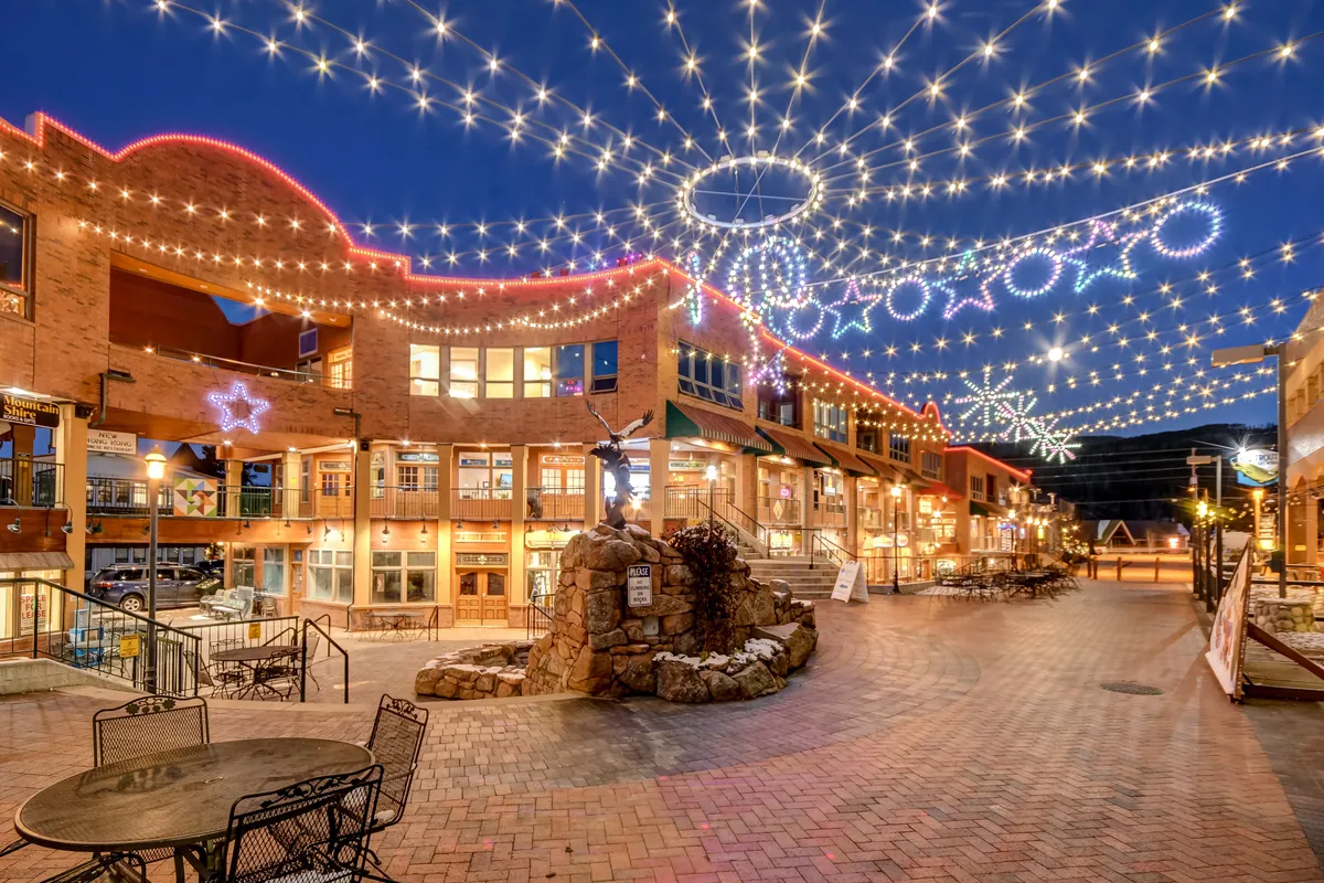 A lively evening scene featuring twinkling string lights, decorative stars, and a central fountain. The space is alive with the energy of potential community gatherings, social events, and festive celebrations under the night sky.