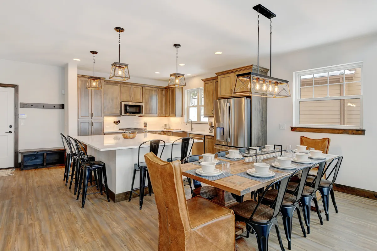 An open-plan kitchen and dining area, spotlighting a central island, adjacent dining table, and elegant light fixtures. The warm, welcoming mood is accentuated by stylish finishes and ample room for guests to mingle or dine.