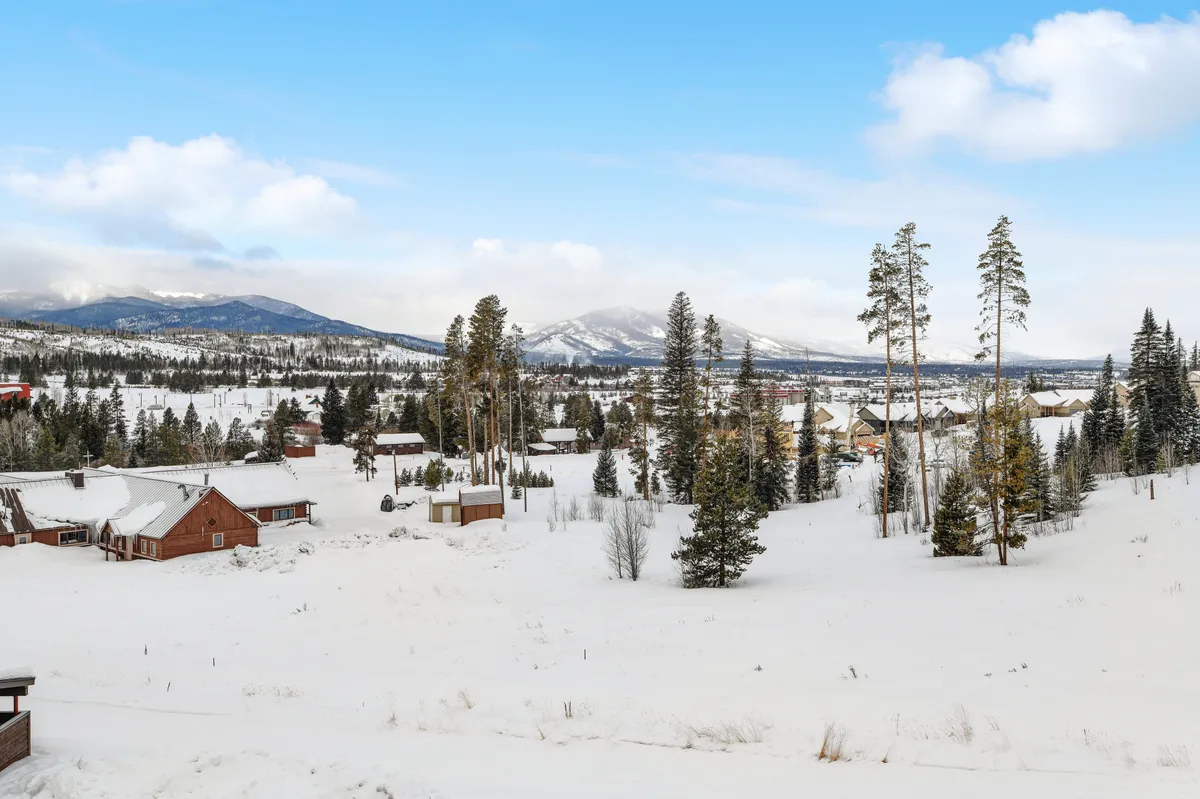 A panoramic view of a snow-covered landscape, distant mountains, pine trees, and scattered cabins. The scene is tranquil and expansive, illustrating the beautiful natural surroundings available for outdoor adventures and exploration.