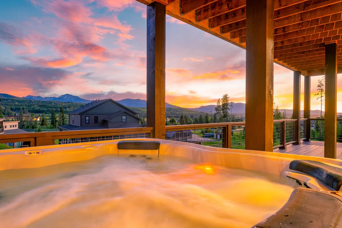 An inviting outdoor hot tub positioned on a deck with a view of the sunset and distant mountains, framed by a sturdy railing. The setting is tranquil and promises ultimate relaxation after a day of adventure.