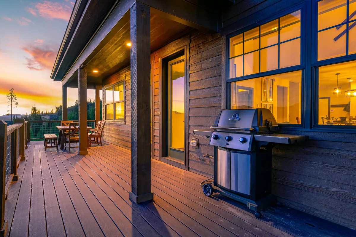 An outdoor deck scene with a dining table, grill, and sweeping sunset views over the Rockies. The setup invites outdoor dining and relaxation, seamlessly extending the living space into nature.