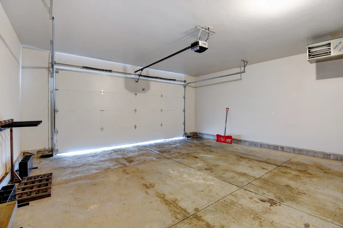 A practical garage featuring a visible garage door, shelves for storage, and tools such as a shovel, providing a sense of ample space for gear storage. The organization hints at room for skis, bikes, boots, and other adventure equipment.