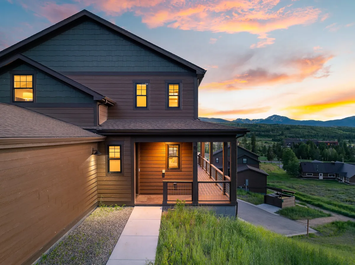This exterior shot showcases the home's striking wooden exterior and a welcoming porch with a railing. The background captures a vivid sunset, inviting the viewer to imagine enjoying outdoor gatherings or quiet moments while surrounded by natural beauty and serenity.