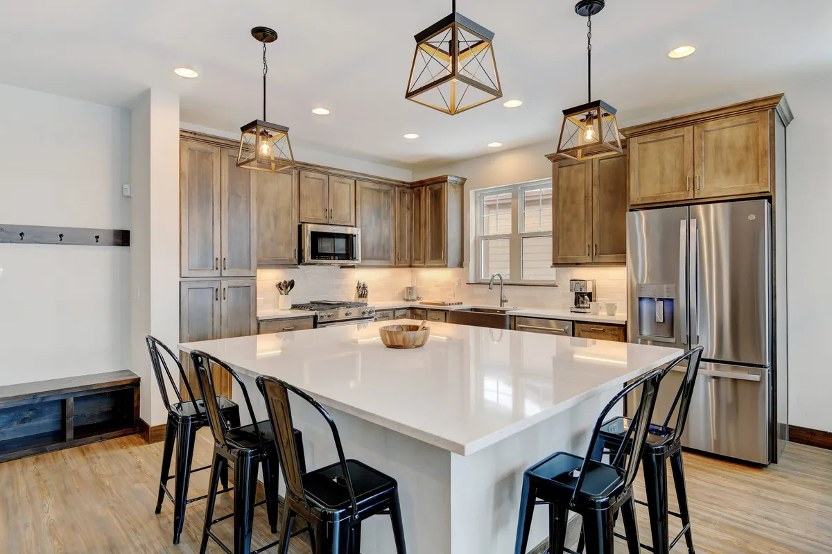 A spacious, modern kitchen featuring a large island with seating, pendant lights, and gleaming stainless steel appliances. The open layout is designed for both cooking and socializing, with ample space for multiple people to gather. The kitchen's style suggests high-end finishes and premium amenities.