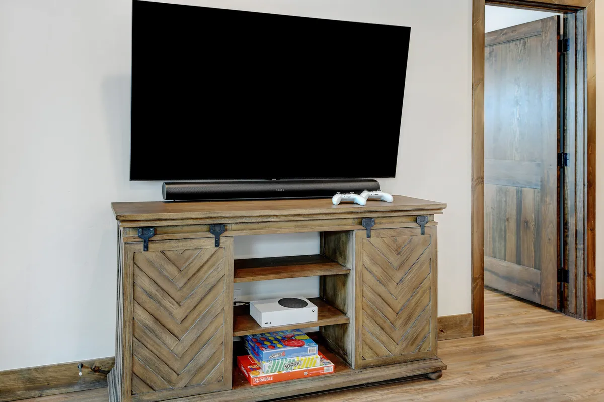 An inviting game and movie room featuring a large TV, a wooden cabinet with a gaming console (Xbox), and a variety of board games. The space includes comfy lounge seating, designed for relaxation and entertainment—ideal for kids and teens to gather, play, and unwind.